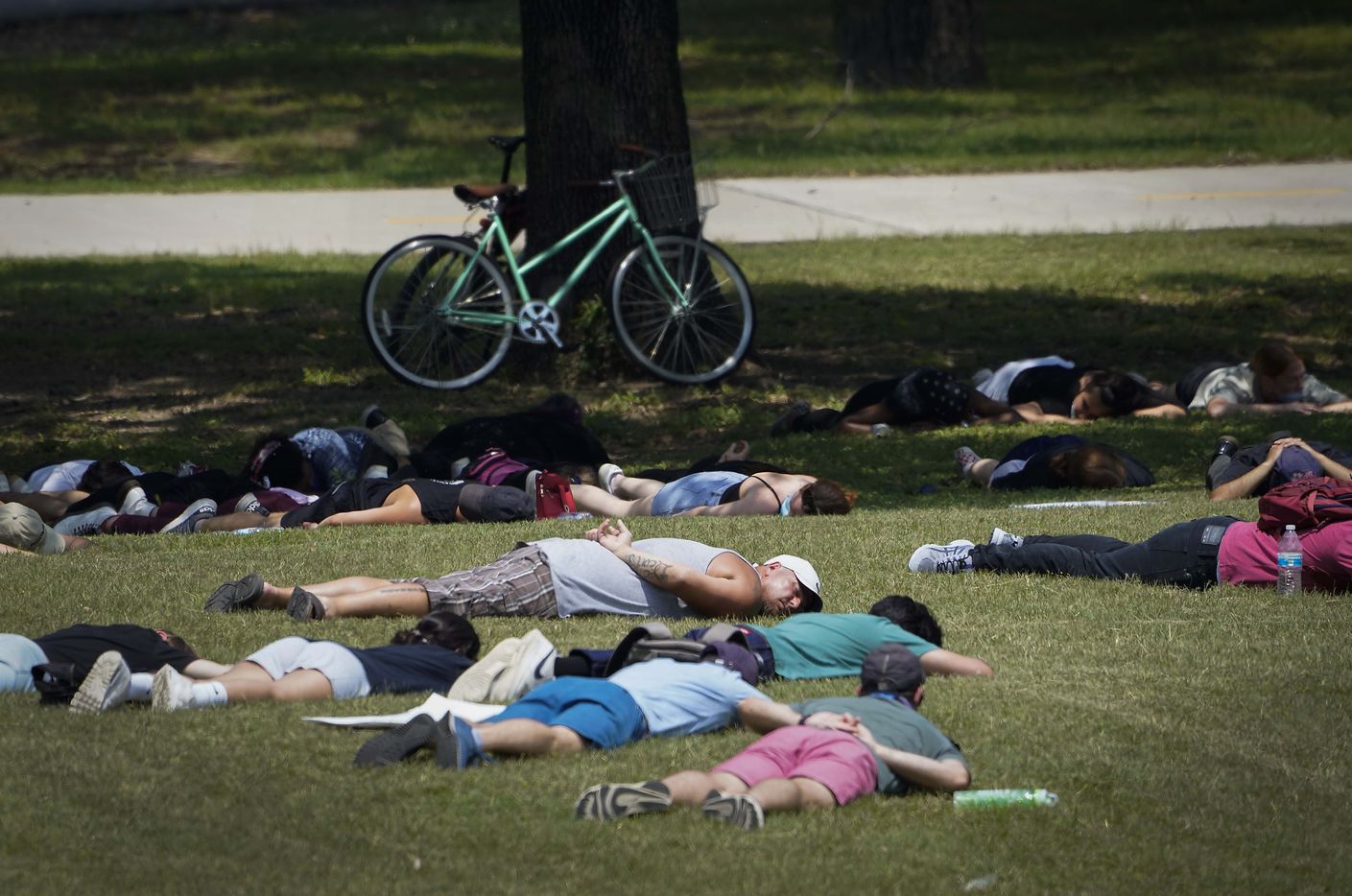 A group of demonstrators lies in the grass, many with their hands behind their backs, at...