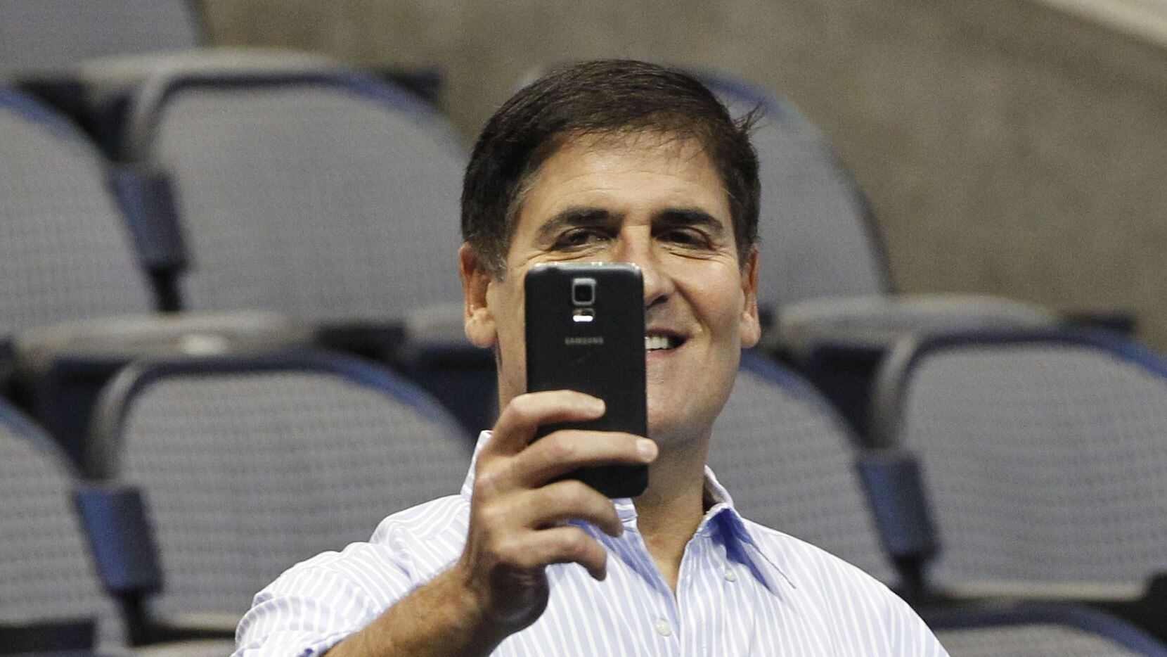 Dallas Mavericks owner Mark Cuban uses his phone prior to the start of a press conference...