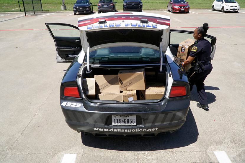 Dallas Police Officer Natasha Meadors loads boxes of hand sanitizer into her patrol car at...