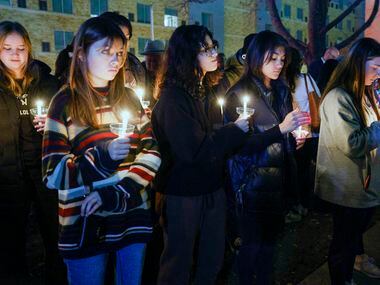 Community members hold candles during the playing of “Amazing Grace” at a candlelight vigil...