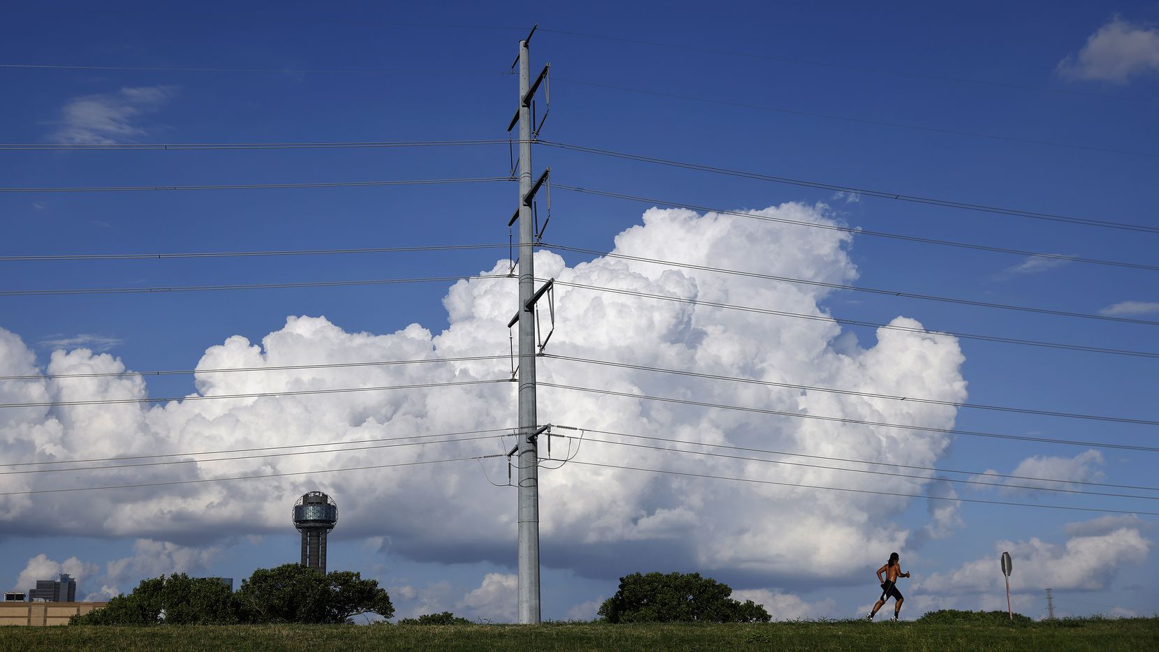A runner on the Trinity River levee passes a large electrical transmissions line near...