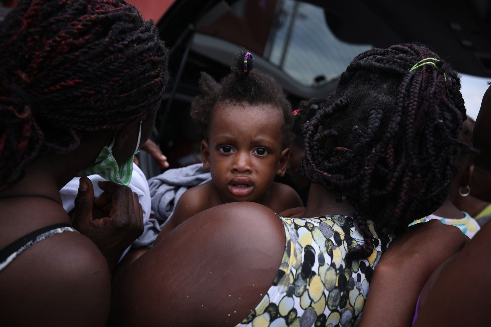 Una niña es cargada en brazos por su madre, mientras ella espera recibir donativos afuera de...