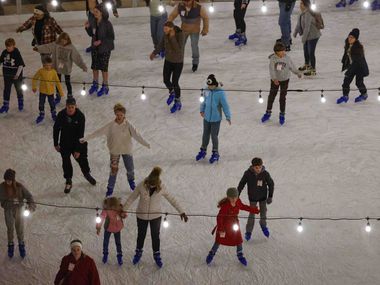 Ice skaters glide underneath strings of lights at the Peace Plaza Ice Rink in front of...