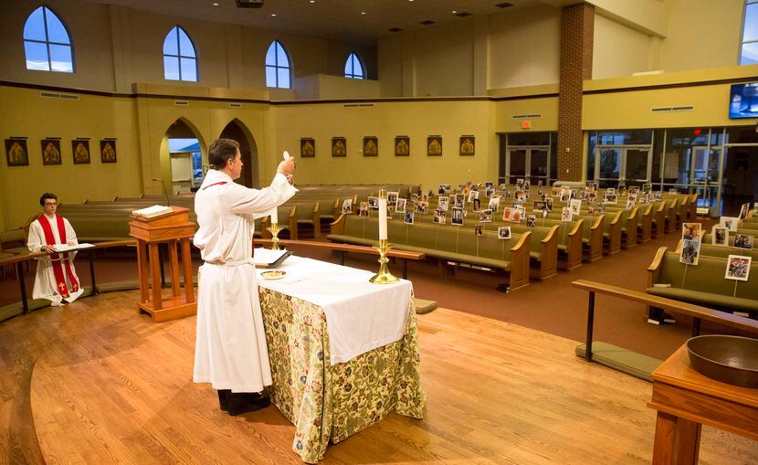 Before a sanctuary full of parishioners photos, Father Clayton Elder holds the eucharist and...