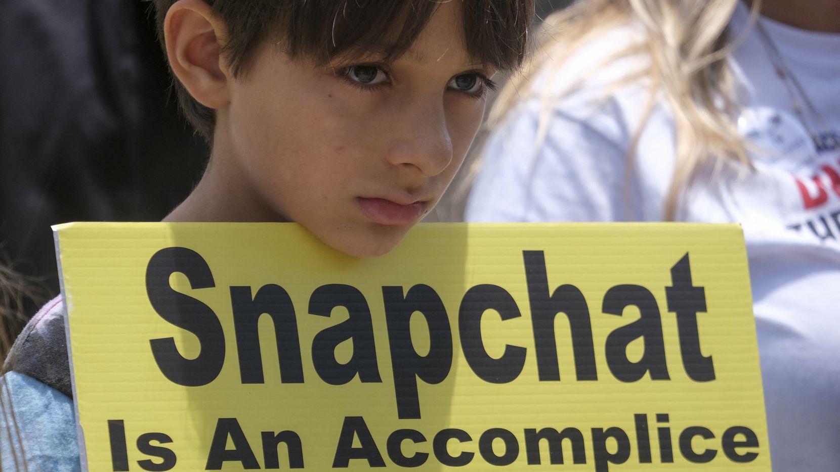 A young person holds a sign as people opposed to the sale of illegal drugs on Snapchat...