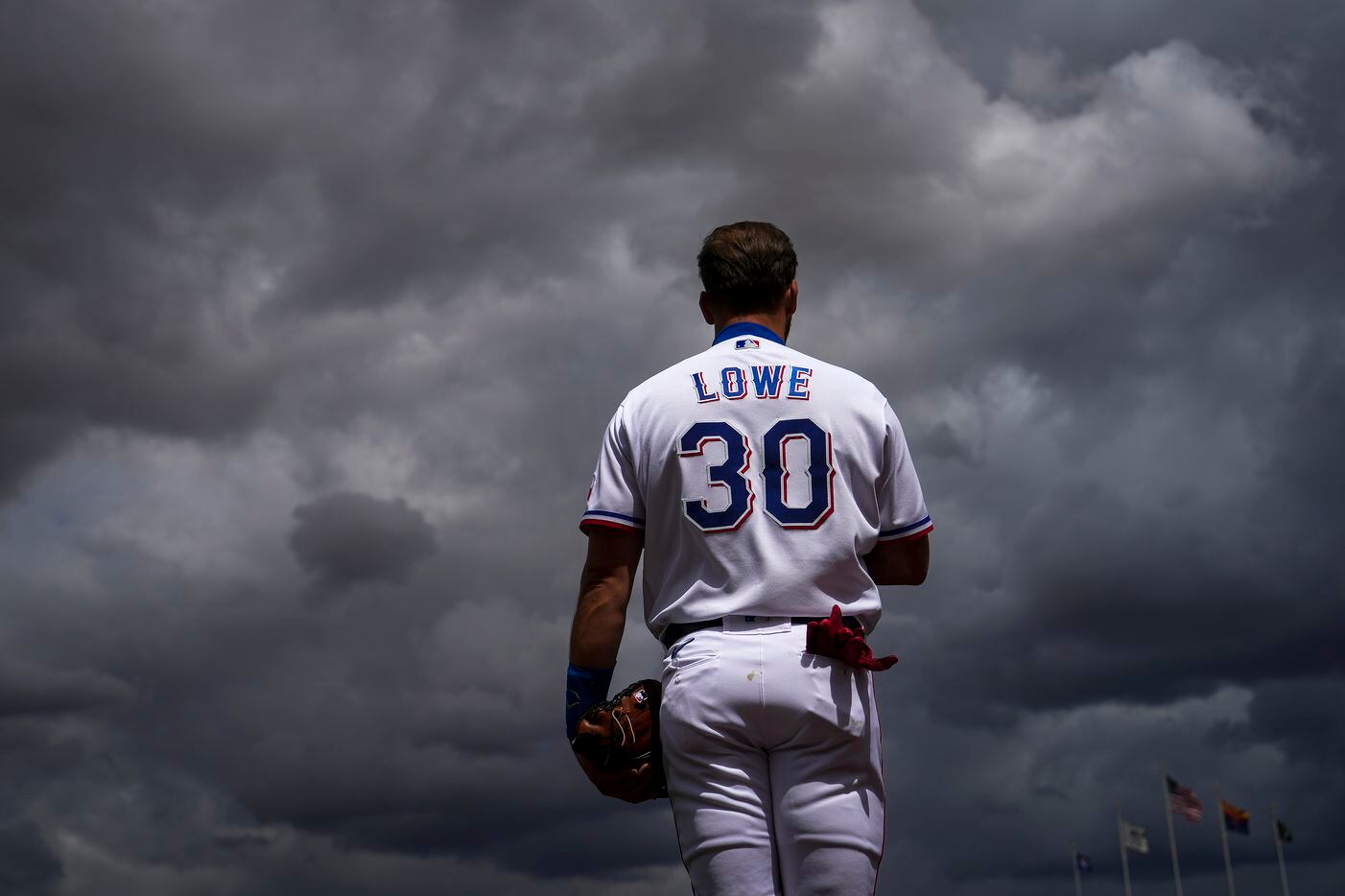 Texas Rangers infielder Nathaniel Lowe stands for the national anthem as clouds from a...