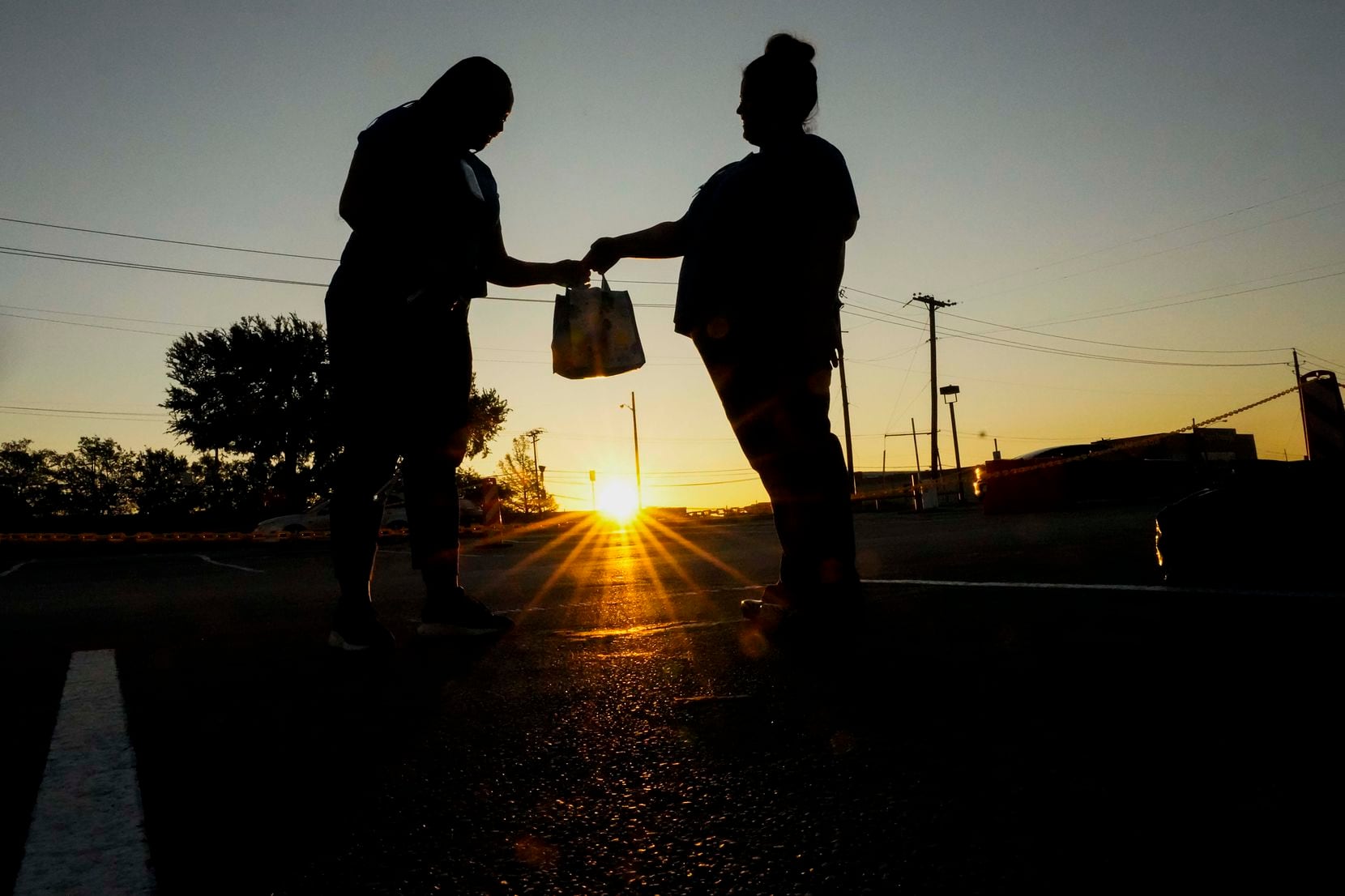 Parkland Homeless Outreach Medical Services (HOMES) program nurse manager Dolores Diaz (right) hands a gift to colleague Nicoya Hutcherson at they arrive for work at 7:00 a.m. as the sun rises at a COVID-19 drive-through testing site at the hospital on Thursday, April 23, 2020. (Smiley N. Pool/The Dallas Morning News)