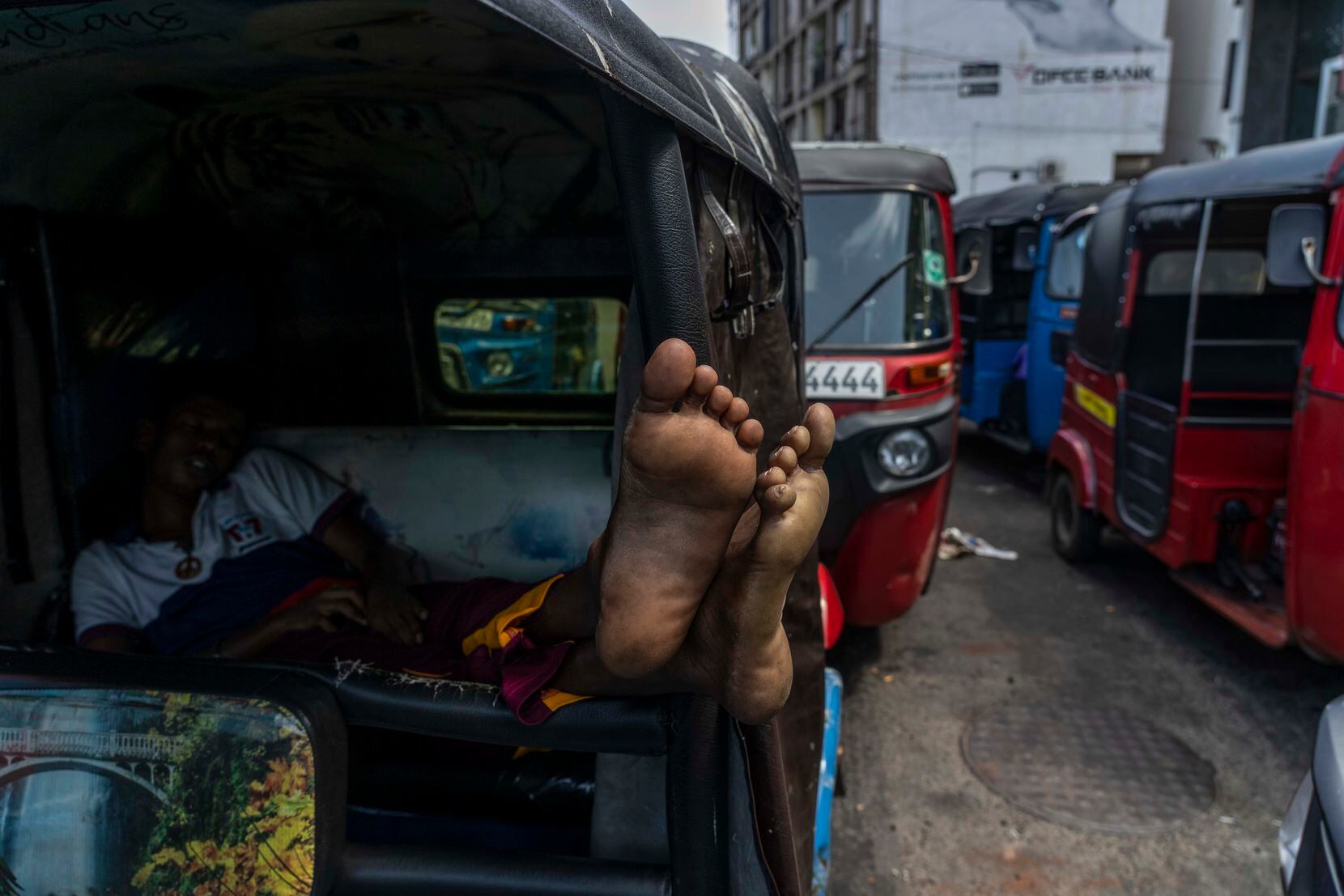 A driver of an autorickshaw sleeps inside his rickshaw while waiting in a queue to buy...