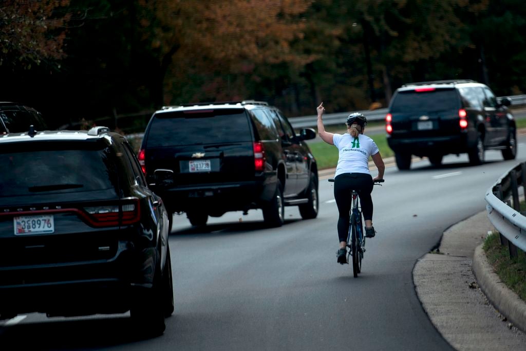In this Oct. 28, 2017, photo Juli Briskman shows her middle finger as a motorcade with President Donald Trump departs Trump National Golf Course in Sterling, Va. After losing her job with a federal contractor after the photo went viral, she entered politics. On Nov. 5, 2019, she won a seat on the Loudoun County Board of Supervisors.