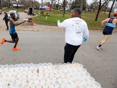 Cliff Piper (center) gives water to runners at the 17-mile mark of the BMW Dallas Marathon...