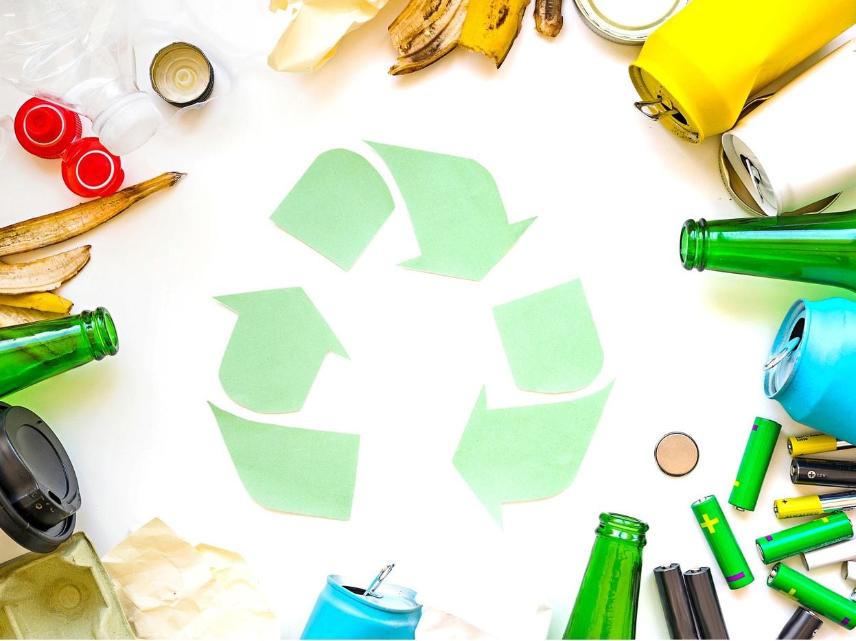 Foto de un logo de reciclaje y botellas de plástico, una botella vacía entre otra basura.