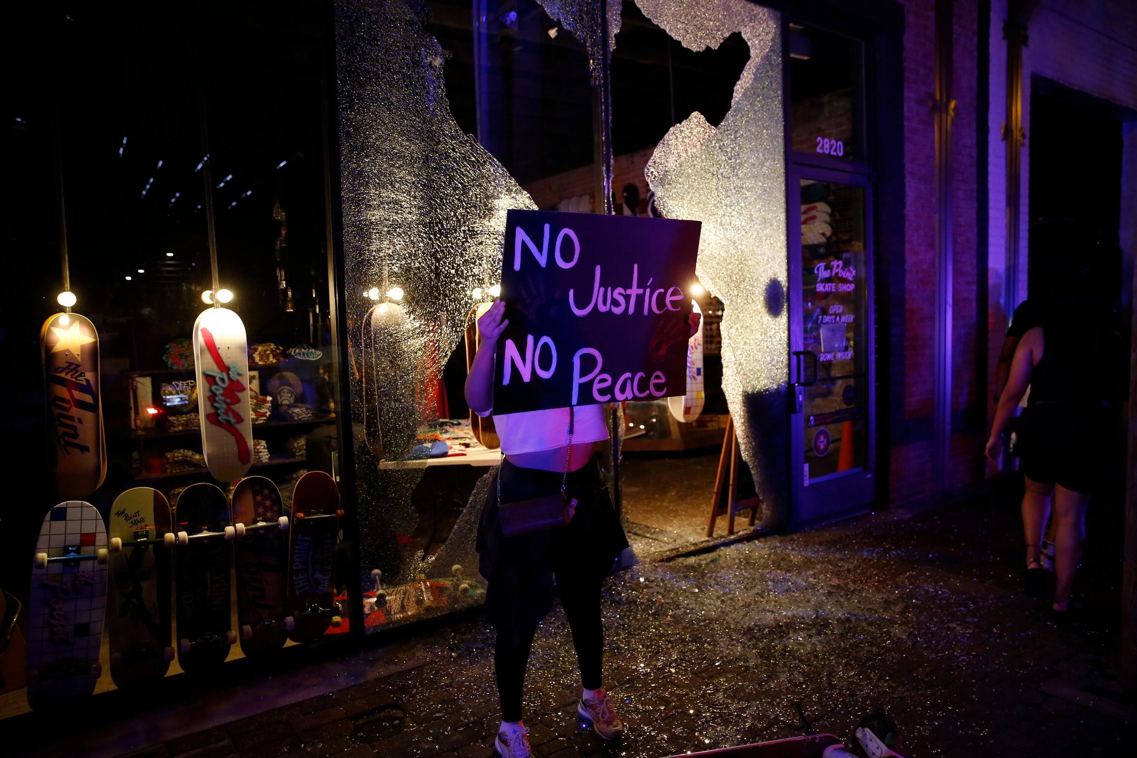 A protestor passes by broken windows along Main Street in Deep ellum after protesters passed...