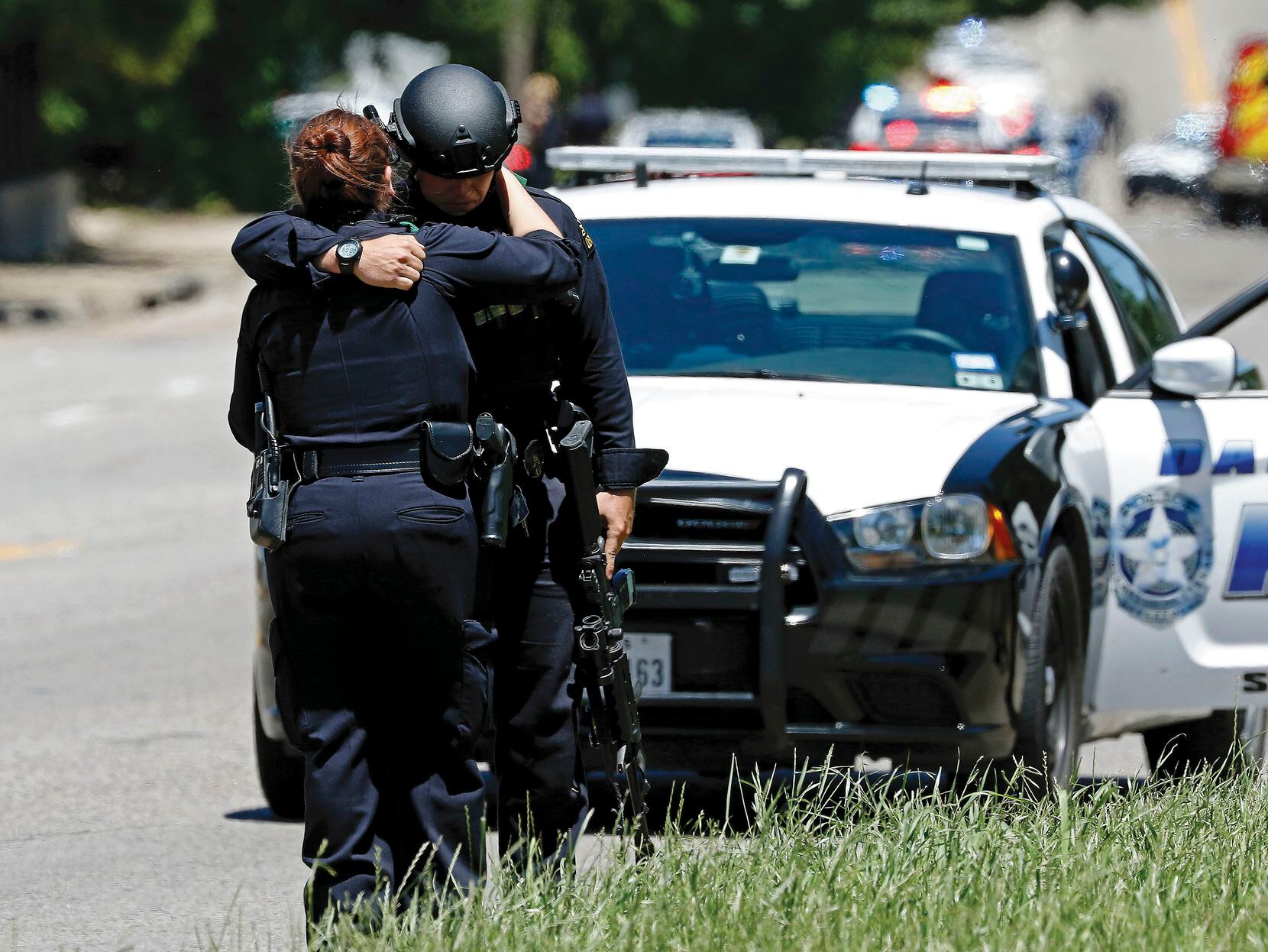 Two Dallas police officers comfort each other at a shooting scene on Dolphin Road where a Dallas Fire-Rescue paramedic nearly lost his life to a suicidal gunman. The paramedic, William An, spent almost a month in the hospital.
