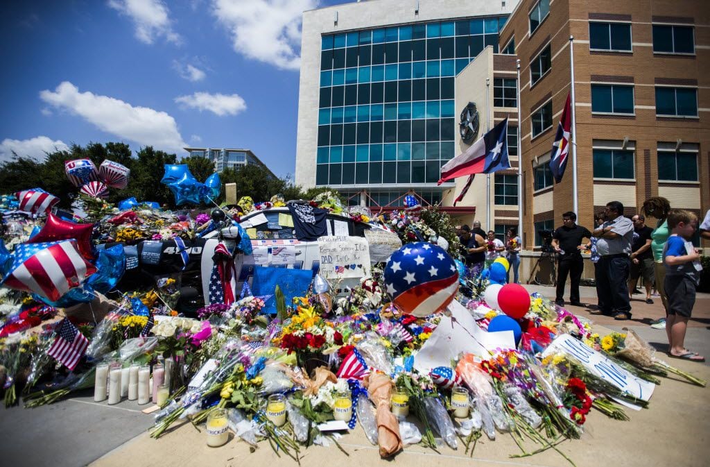 A growing memorial surrounded Dallas police vehicles on Sunday outside police headquarters...