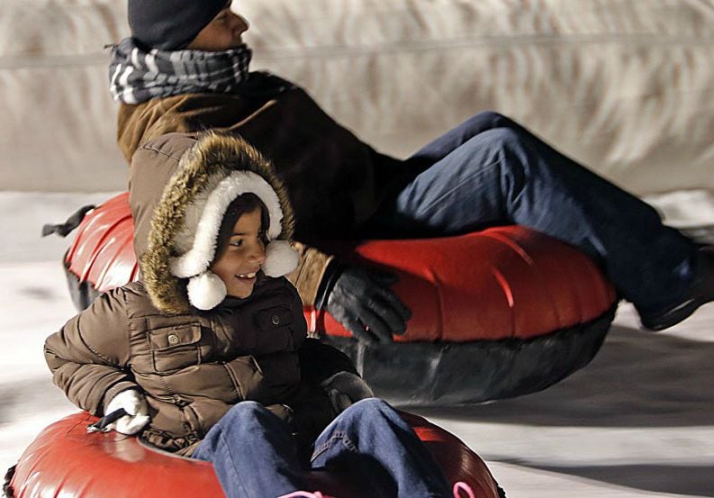 Mia Cardona slides next to her father on a snow slide.