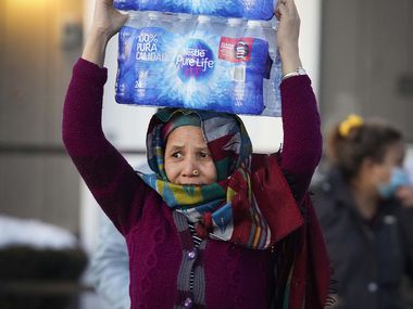 A woman carries two cases of drinking water distributed at the Literacy Achieves nonprofit in Vickery Meadows to nearby residents living without water after a winter storm brought snow and continued freezing temperatures to North Texas on Thursday, Feb. 18, 2021, in Dallas.