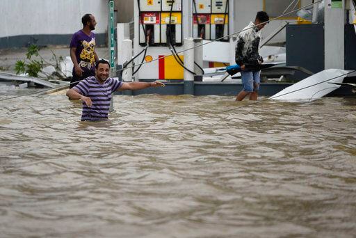 Varias personas caminan cerca de una gasolinera inundada y dañada tras el paso del huracán...