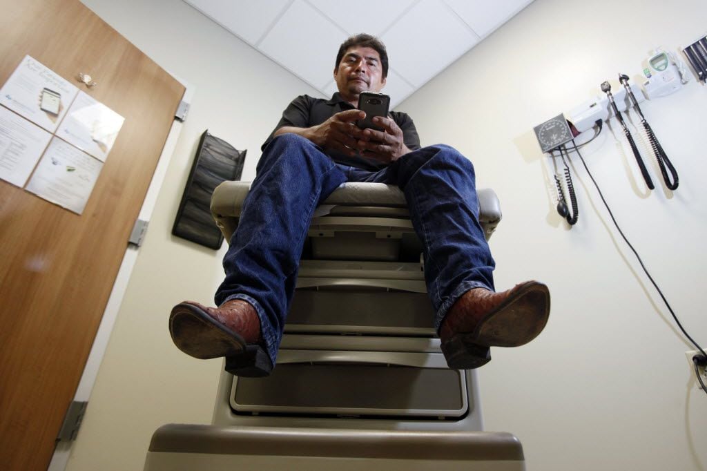 Rodrigo Garcia, 40, of Wylie, holds his cell phone while sitting on a examination table...