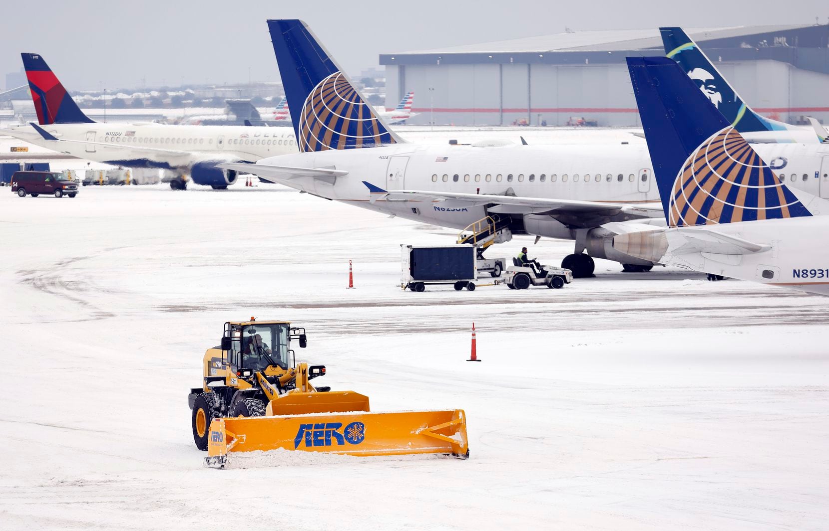 Crews use plows to clear snow from the Terminal B tarmac at Dallas-Fort Worth International...