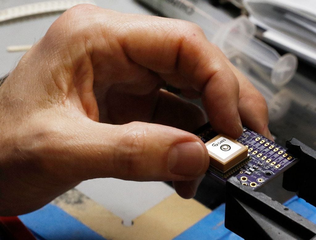 Jesse Hammer, chief engineer & co-founder of Kubos, places a GPS chip on a printed circuit board at Kubos in Denton.