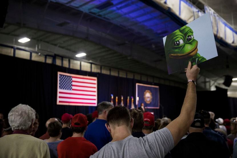 An attendee at a Trump rally in New Hampshire holds a sign featuring Pepe the Frog, a...
