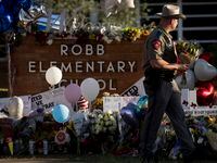 An officer carries flowers to the sign outside of Robb Elementary School where a Tuesday...