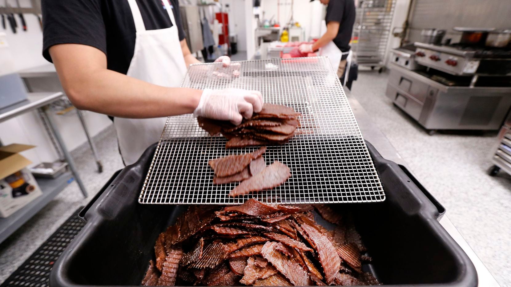 Frick Chanthorn removes warm beef jerky slices from the dehydration unit and piles them into...