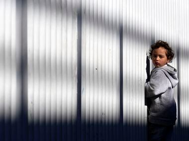 Un niño migrante de pie junto a una cerca en un punto de entrada para solicitantes de asilo...