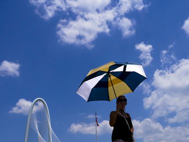 Vimarie Rivera shields herself from the sun under an umbrella as she walks on the Ronald...