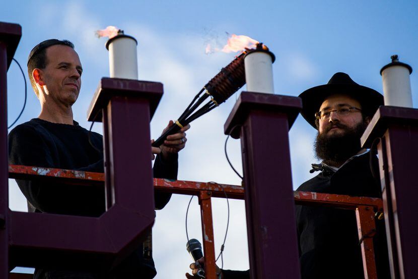 Evan Bundis, left, and Rabbi Moshe Naparstek, right, light the menorah at the Aaron Family...