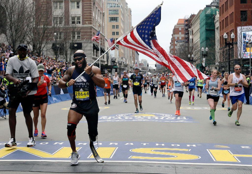 Jose Sanchez, of San Antonio, carries the United States flag across the finish line in the...
