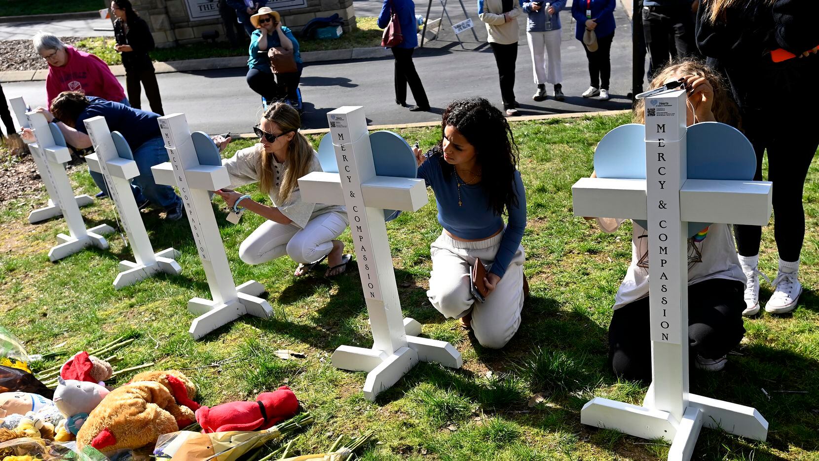 People gather to sign wooden crosses placed at a makeshift memorial by the entrance of the...