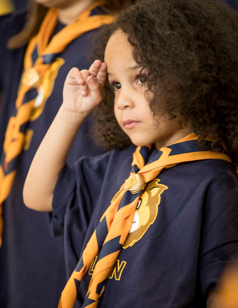 A young Cub Scout stands in uniform to salute with her fellow Scouts.