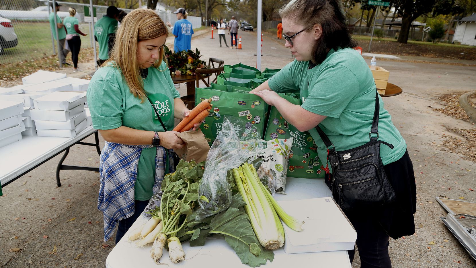 Whole Foods volunteers Christie Streit and Arael Byrd (right) place produce from Restorative Farms into bags in Dallas on Sunday, Nov. 21, 2021.