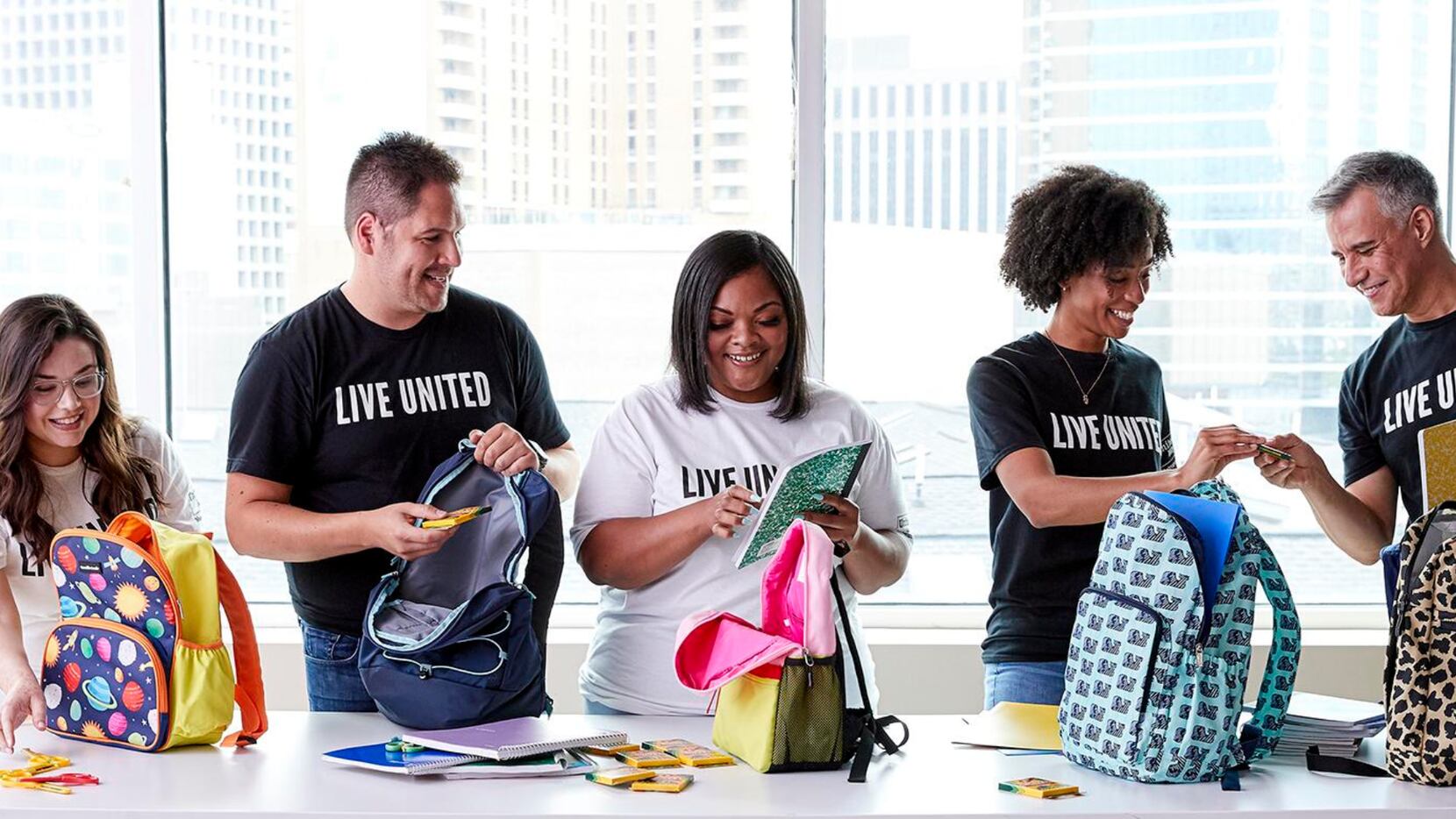 Five people packing backpacks while volunteering with United Way, wearing Live United shirts