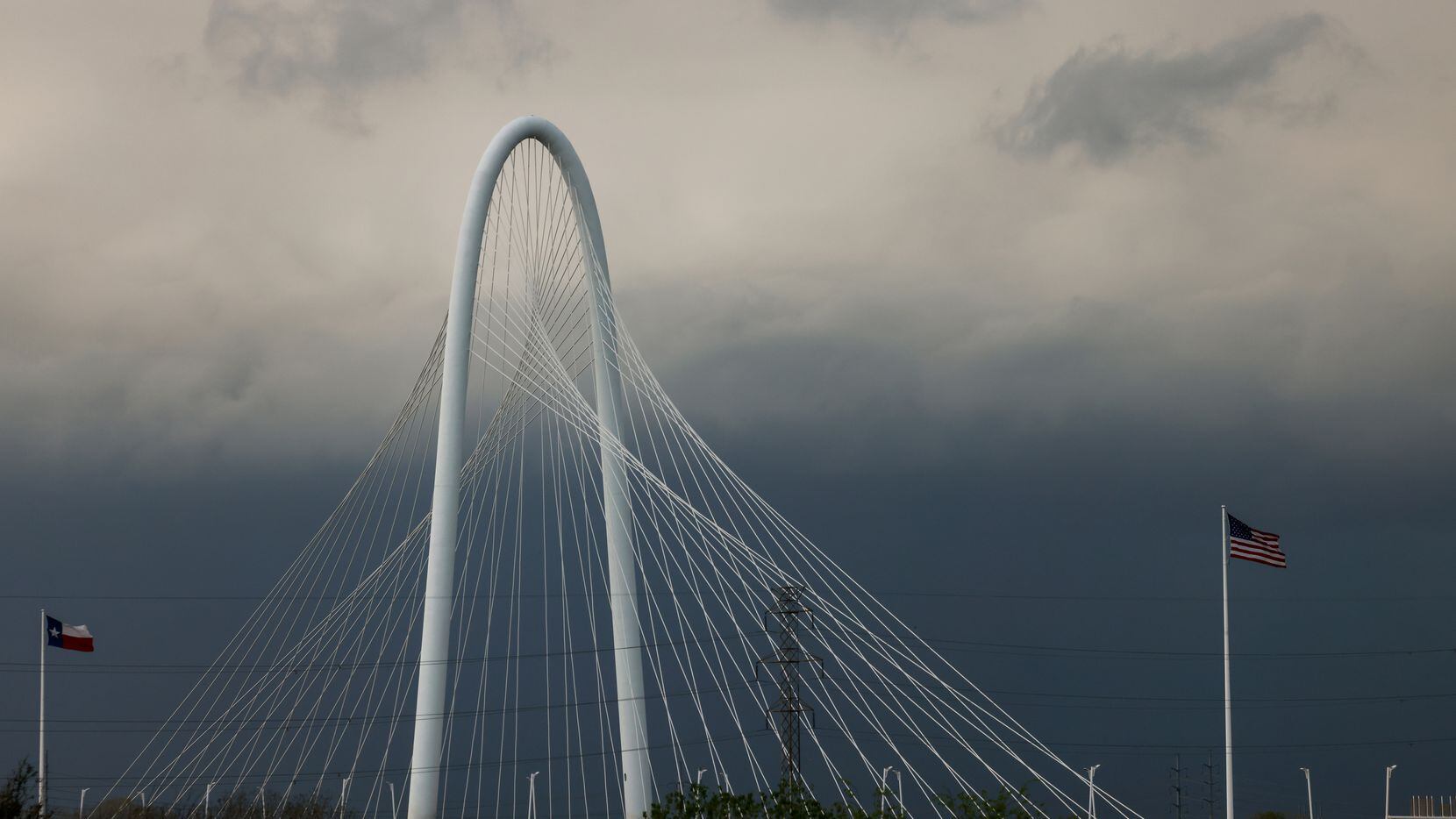 Flags on Margaret Hunt Hill Bridge ripple in the wind as storm clouds move toward downtown...