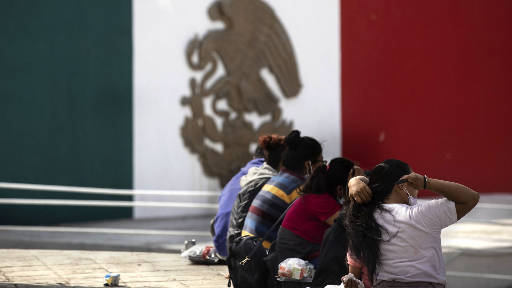 A migrant woman brushes her hair as she and other expelled migrants sit at a plaza near the...
