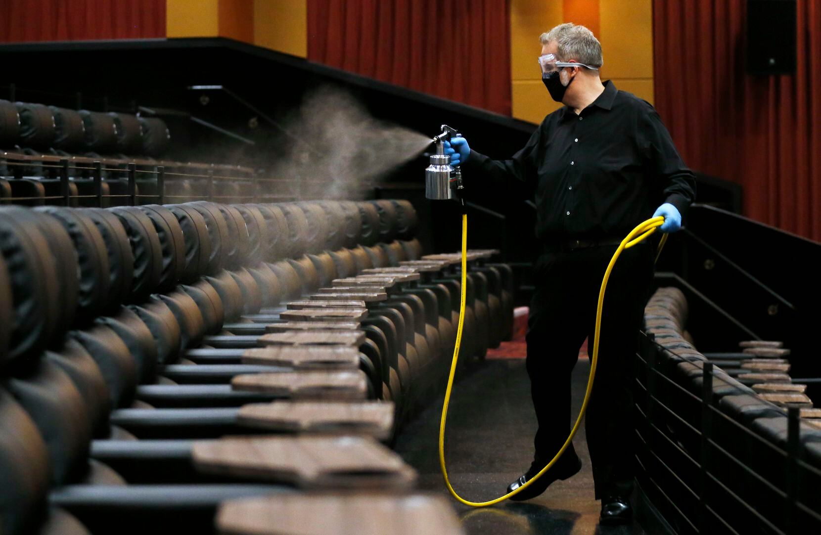 Cinemark West general manager Lindsey Hearn sprays disinfectant on seats in an auditorium the morning before they reopen at Cinemark West in Plano, on Friday, June 19, 2020. After being closed for months due to the coronavirus pandemic, the theater is reopening Friday. (Vernon Bryant/The Dallas Morning News)