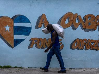 Un trabajador carga un saco de arroz frente a una pinta en la calle que dice "A Cuba ponle...