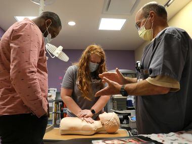 Stephanie Brooks (center) practices CPR on a dummy to the beat of paramedic Brad Nance’s...
