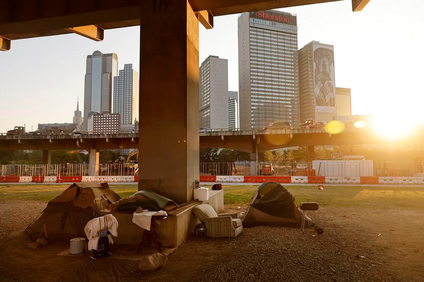 The sun sets behind a homeless encampment under the I-345 overhead in downtown Dallas,...
