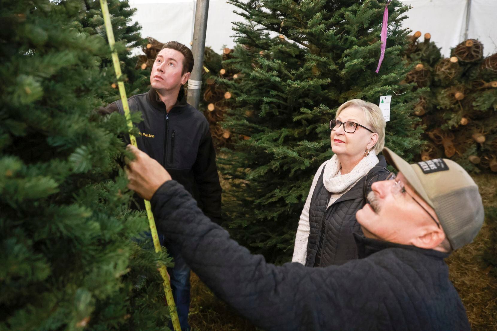 Owner John Patton and Candace Cain watch as Brian Cain measures the height of a Christmas...