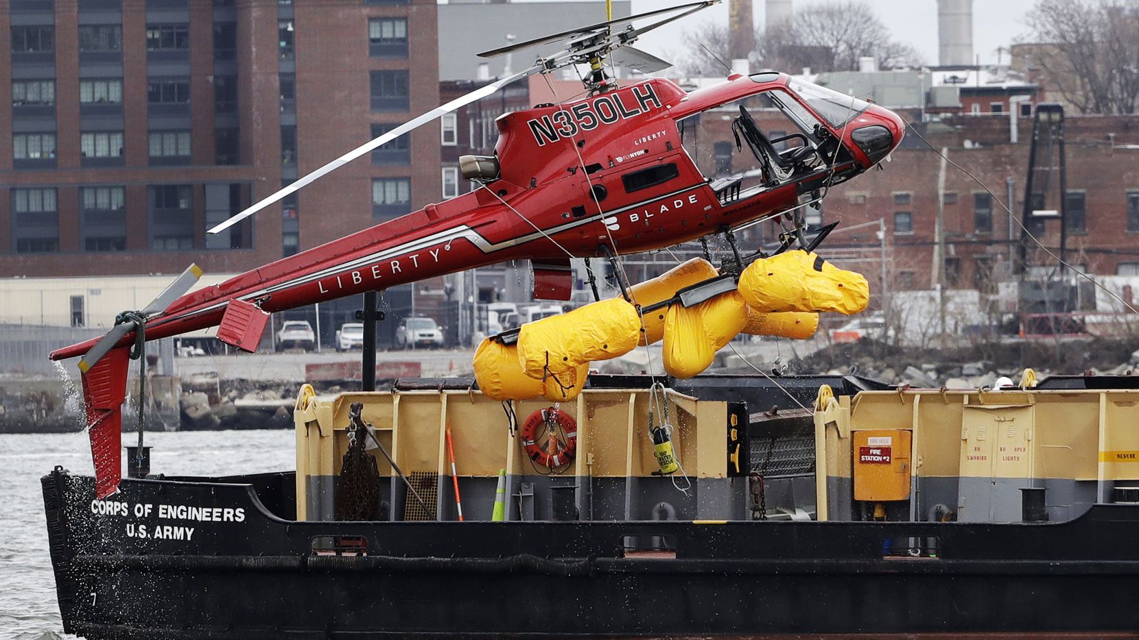A helicopter is hoisted by crane from the East River onto a barge, Monday, March 12, 2018, in New York. The pilot was able to escape the Sunday night crash after the aircraft flipped upside down in the water killing several passengers, officials said. (AP Photo/Mark Lennihan)