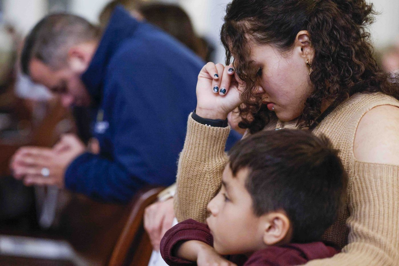 Giselle Huerta sitting by her son Abdel Monasterio, 7, kneels as she prays during a memorial...