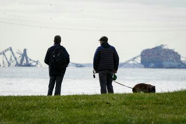 Two men observe the collapsed Francis Scott Key Bridge wreckage from Ft. McHenry, Md., on...