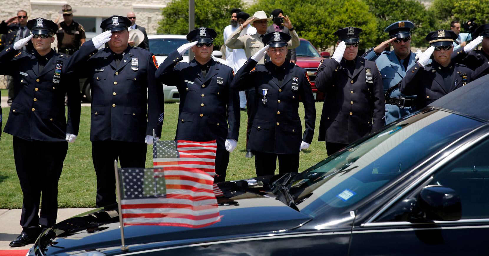 Police officers salute as the hearse passes in the funeral procession for fallen Dallas...