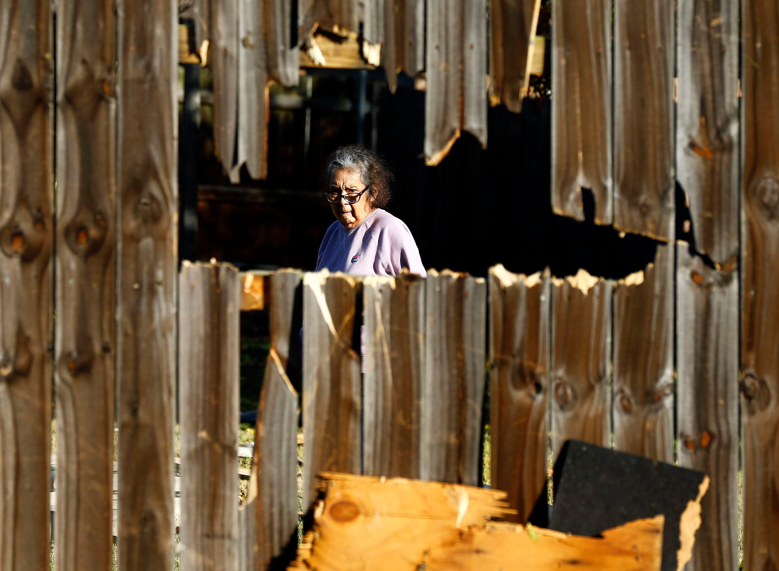 A woman looks through the hole in her fence as she inspects the damage in her yard following...