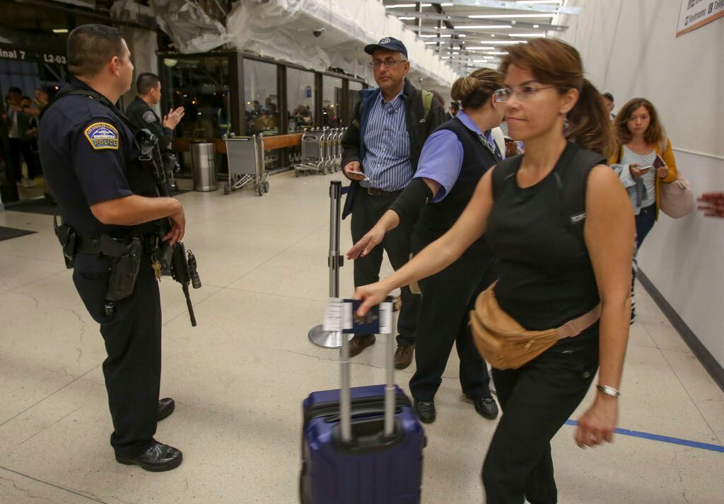 A police officer stands guard as passengers wait in line at Terminal 7 in Los Angeles...