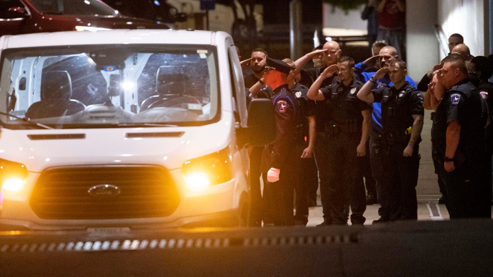 Officers salute as a Mesquite police officer’s body is loaded into a van outside Baylor University Medical Center at Dallas on Friday evening.