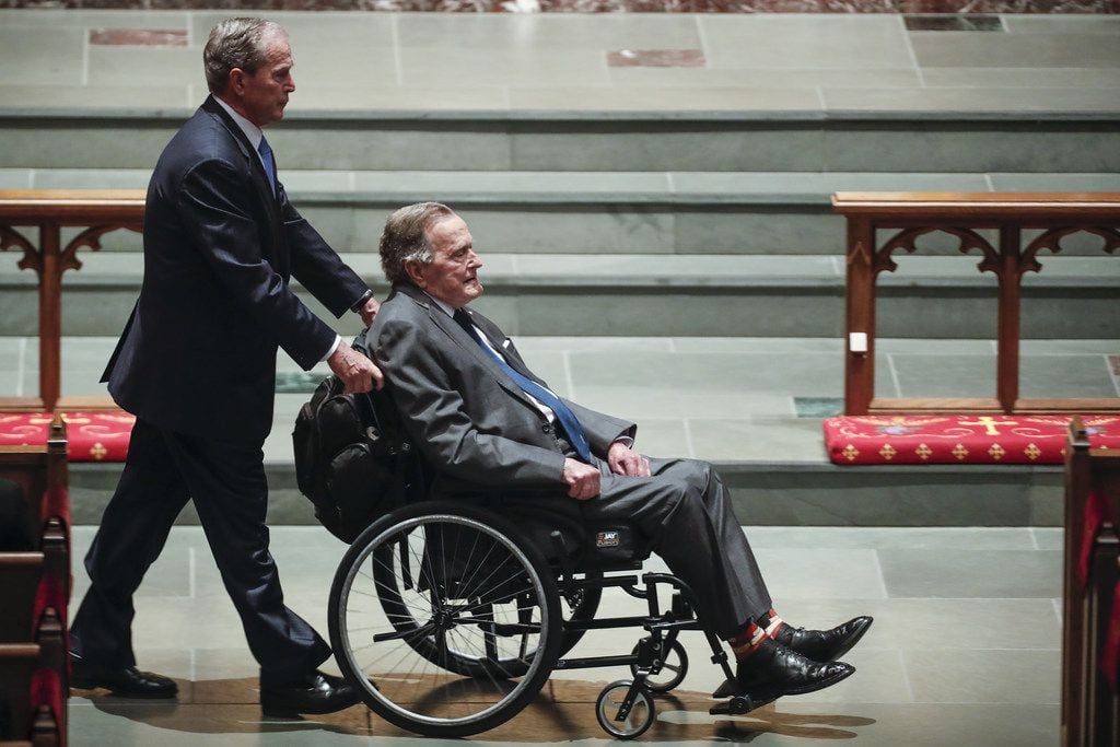 Former president George W. Bush wheels his father, former President George H.W. Bush, into...